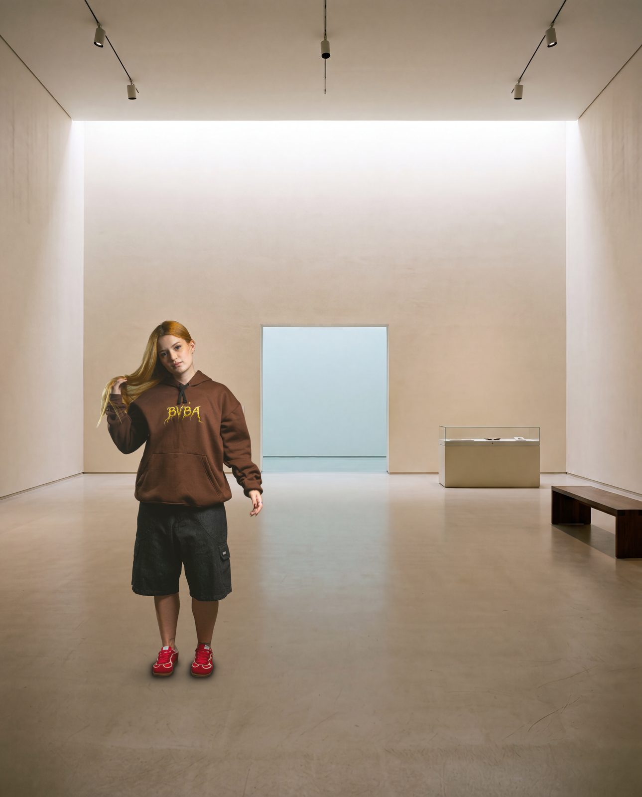 Modelo de moletom marrom BVBA em pé numa galeria clara, com um vão de céu na parede do fundo
